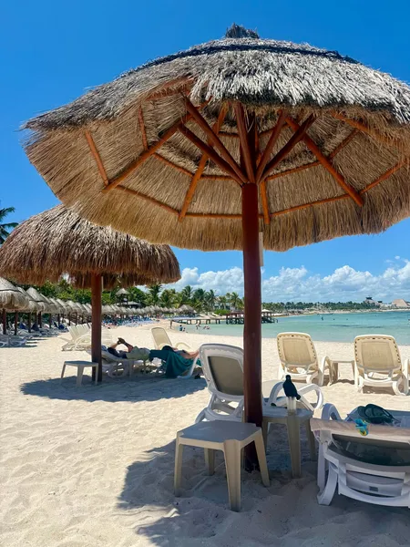 Thatched palapa umbrellas and empty loungers on a white-sand beach beside turquoise water.